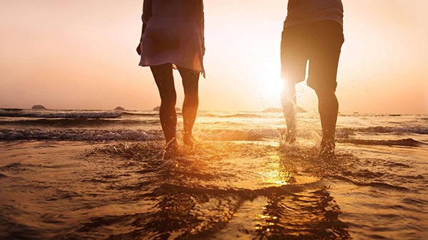 Пара гуляет по пляжу на закате.