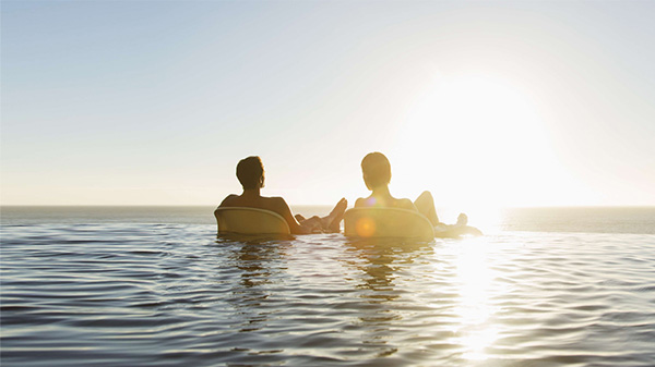Пара отдыхает на шезлонгах у пейзажного бассейна с видом на море.