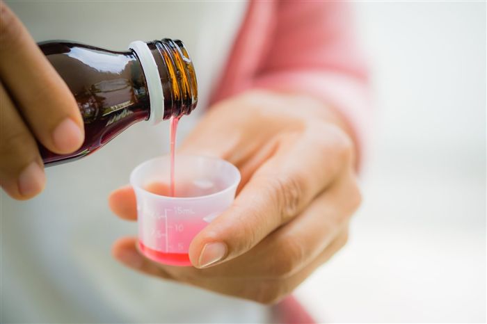 Закрыть женщины, которые выливают сироп с лекарственными средствами и антифрамотиком в чашку из бутылки.