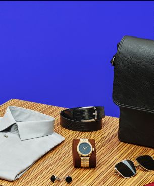 Изображение рубашки, часов, пуговиц на манжетах, ремня и солнцезащитных очков рядом с кожаным портфелем.