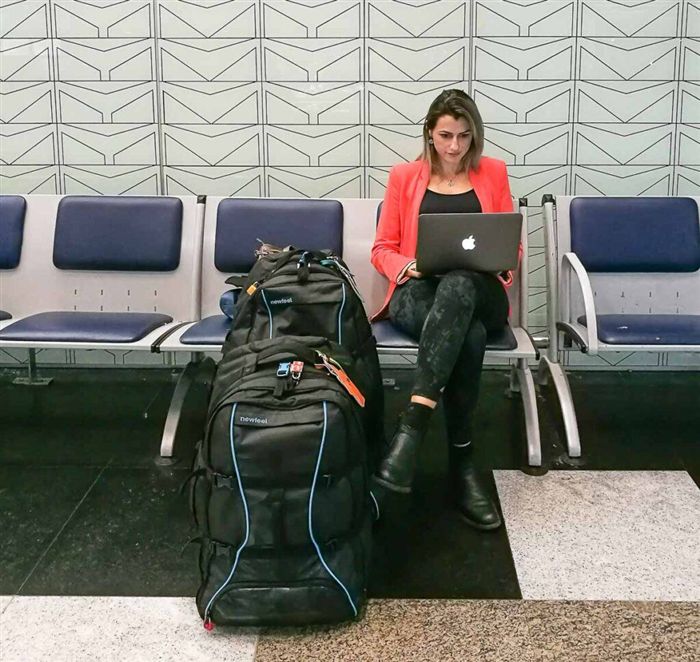 Женщина с ноутбуком в аэропорту. Она подключается к Интернету через Wi-Fi в аэропорту и работает онлайн. Это одно из преимуществ путешествия с ноутбуком.