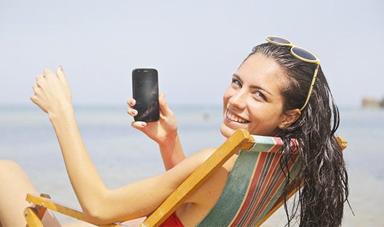 Женщина сидит на пляже и держит мобильный телефон